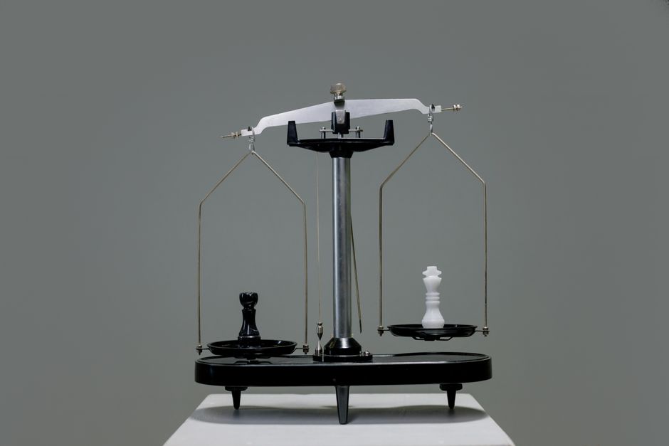 A balance scale weighing two stacks of coins on a wooden desk.
