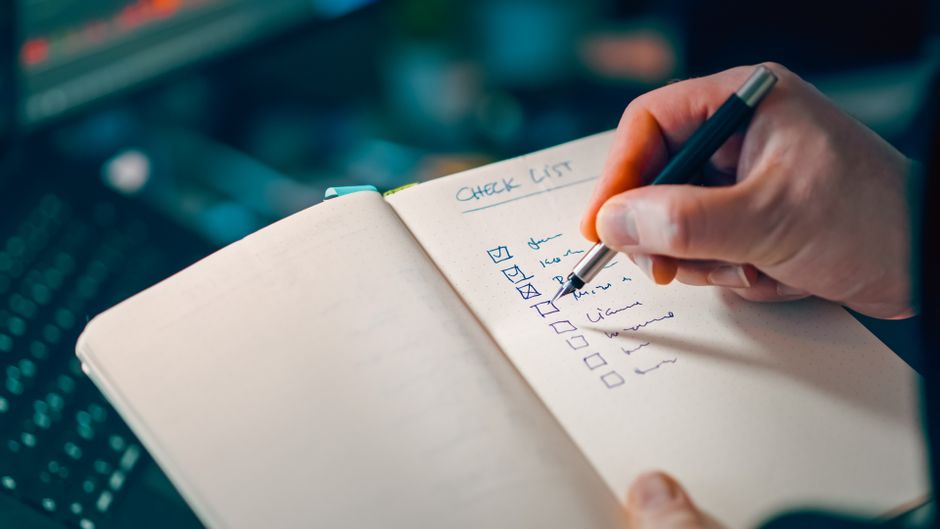 An open notebook on a desk with a person writing a checklist.
