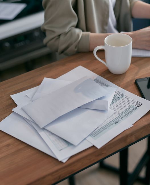 A pile of letters and envelopes stacked on a wooden desk.