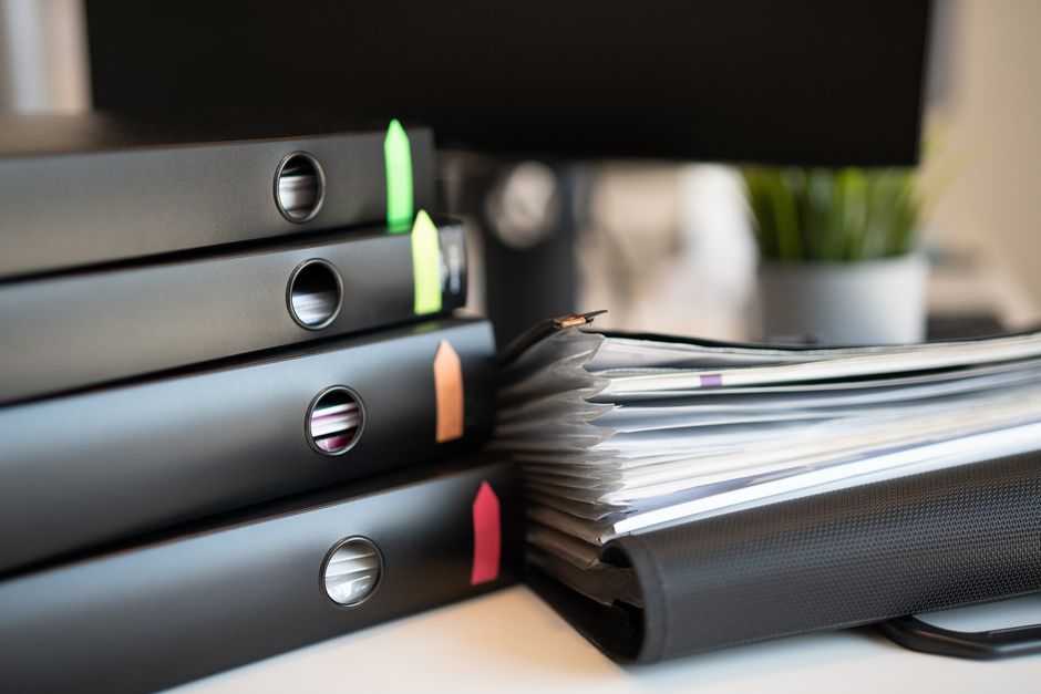 A stack of compliance binders next to a laptop on a desk.